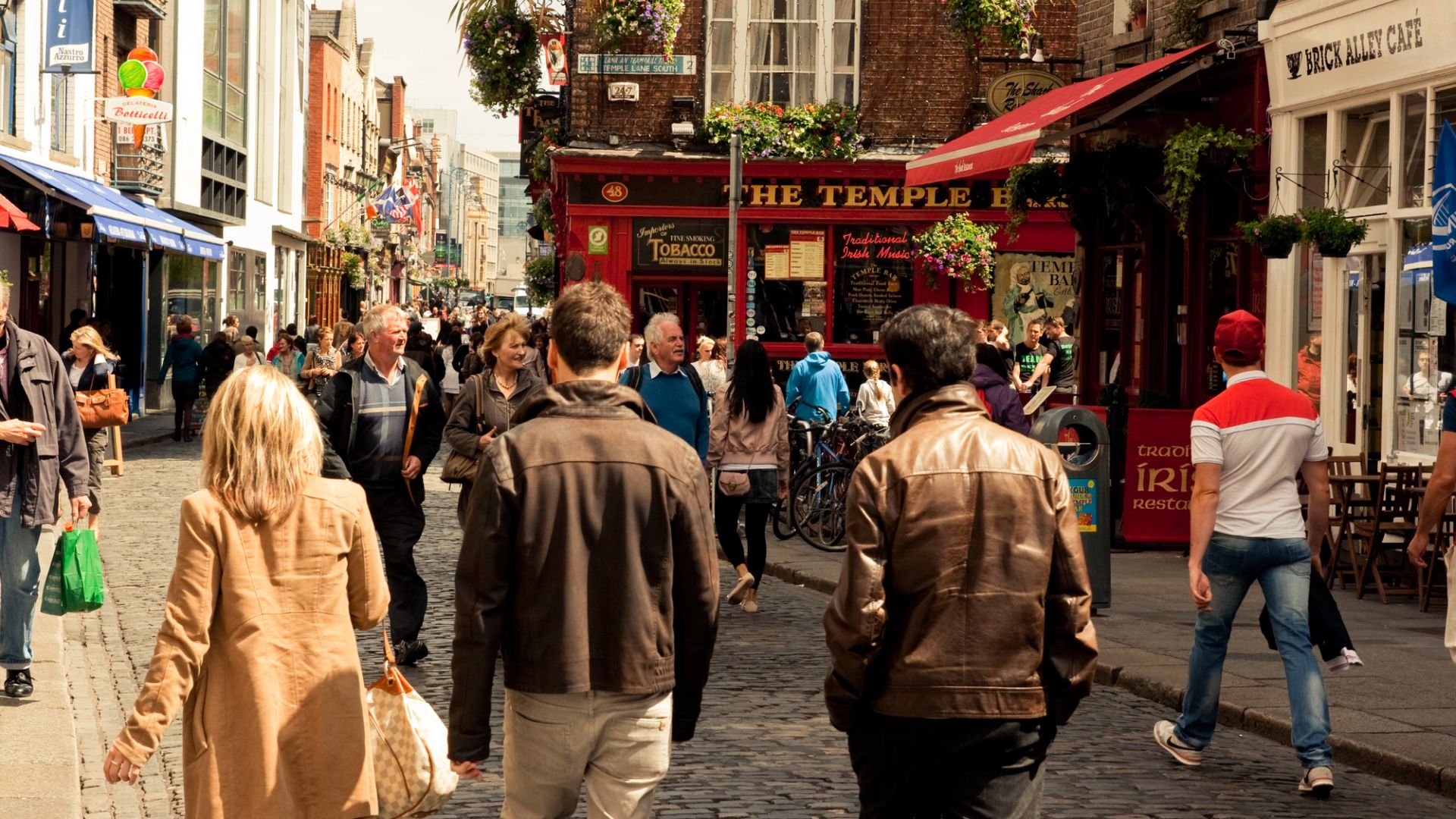 Pedestrians on a street in Dublin approach The Temple Bar with its distinct red facade.